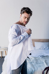 handsome sleepy man dressing white shirt in bedroom at home
