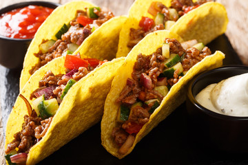 Delicious tacos stuffed with minced beef and vegetables served with sauces close-up on a slate...