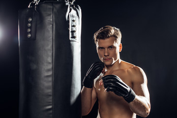 Strong boxer in gloves standing near punching bag and looking at camera