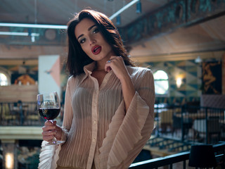 beautiful girl model posing standing with a glass of red wine in her hand in a restaurant