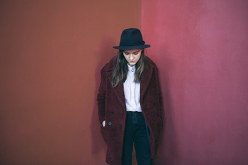 pensive young teen girl stands against the red wall. Sad doubts. Melancholic mood to be alone with...