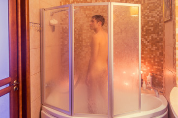 Attractive man in a shower behind a glass screen. Blurred figure of a man taking a shower. 