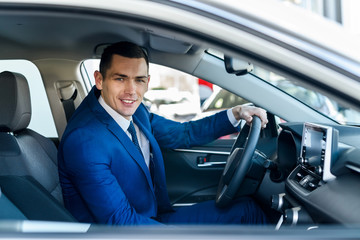 Young and happy businessman sitting in new car in showroom
