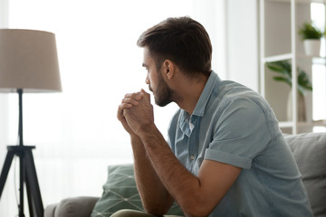 Thoughtful serious man sitting on sofa at home, lost in thoughts