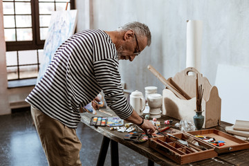 Professional experienced artist standing near the table with paints