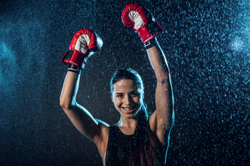 Smiling boxer in red boxing gloves showing yes gesture under water drops on black