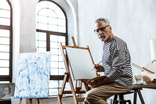 Professional famous artist sitting and painting in big workshop