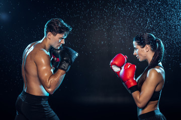 Side view of two boxers in boxing gloves training together under water drops on black - Powered by Adobe
