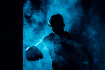 Boxer in boxing gloves training in dark with smoke