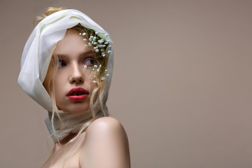 Model with white silk scarf on her head posing near background