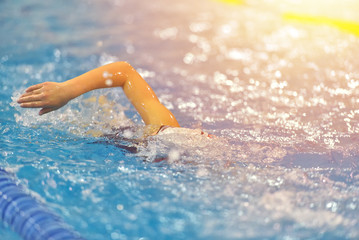 Young girl in swim suit, goggles and cap swimming in the blue water pool