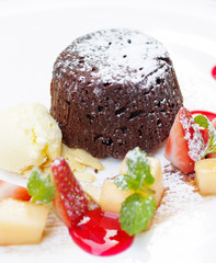 Chocolate lava cake with sugar powder, ice cream, chopped strawberry and apple on white plate