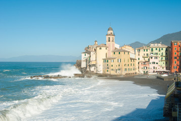 Fototapeta na wymiar Church of Camogli in a day with sea storm that overwhelms beach and pier with blue sky