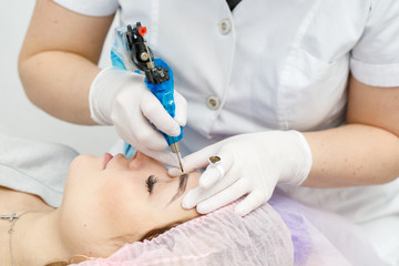 Naklejka premium Permanent makeup, tattooing of eyebrows. Cosmetologist applying make up