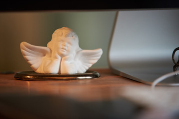 Figur eines kleines Engels steht auf einem Schreibtisch neben einem Computer