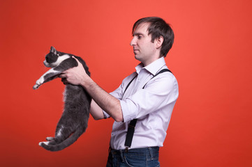 side view of man in shirt with rolled up sleeves holding gray cat on outstretched arms with back side ti himself on orange background with copy space