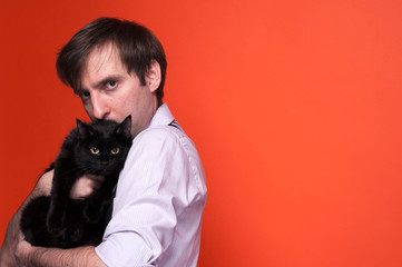 side view of handsome serious man, looking at camera, holding and kissing black cat on orange background with copy space