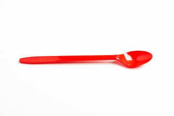 A single long and unused shiny red plastic spoon deliberately and artistically set on a plain white background.