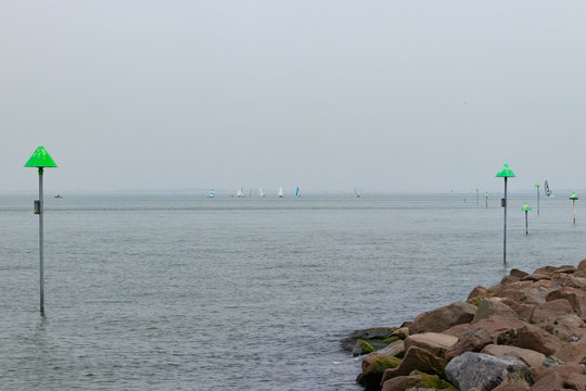 sailing boats on horizon and navigation markers with stones on foreground 