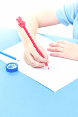 Hands of a child on desk with a red pencil with V sign and a blank white sheet on blue background. With copy space for back to school, writing and education concept - obrazy, fototapety, plakaty