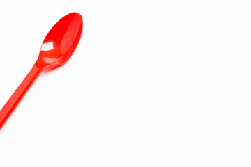 A single long and unused shiny red plastic spoon deliberately and artistically set on a plain white background.