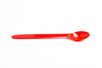 A single long and unused shiny red plastic spoon deliberately and artistically set on a plain white background.