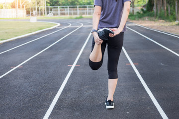 Fitness concept. Young fitness woman stretching legs and preparing to run on the floor at stadium
