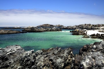 View on natural turquoise pool surrounded by jagged rocks with altostratus clouds in the horizon - Bahia Inglesa at pacific coast of Atacama desert, La Piscina (The Pool)