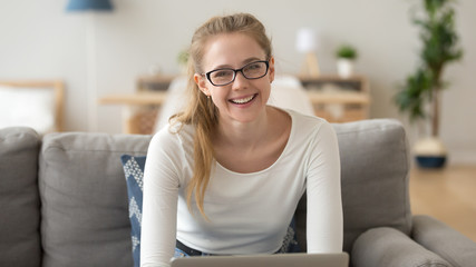 Head shot portrait of smiling woman in glasses, sitting on sofa at home