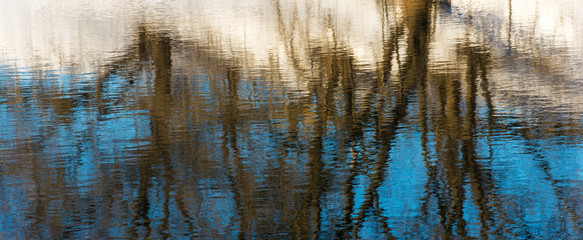 Beautiful reflection of trees in the blue mirror smooth surface of the river.
