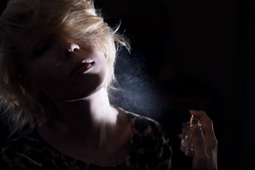 Woman puts on perfume on a dark background.