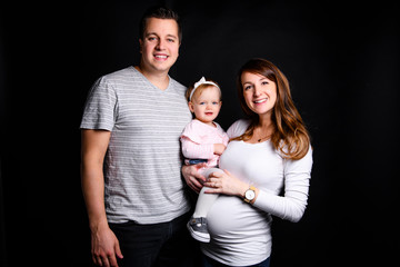 A beautiful happy family with a pregnant mother over black background