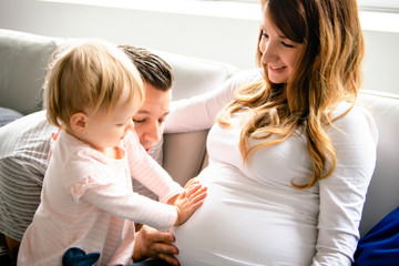 A Beautiful pregnant mother and father with her children girl at the living room