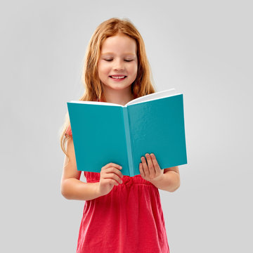 childhood and people concept - smiling red haired girl reading book over grey background