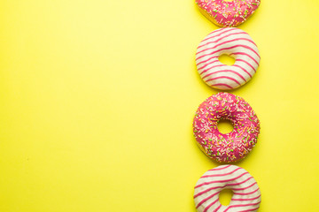 Assorted colorful donuts on yellow background, pink glazed and sprinkles donuts. Dessert, sugar food concept