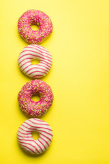 Assorted colorful donuts on yellow background, pink glazed and sprinkles donuts. Dessert, sugar...