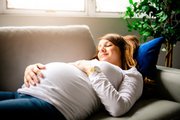 A happy pregnant woman lying on sofa at home