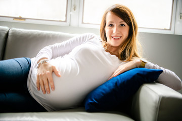 A happy pregnant woman lying on sofa at home