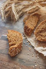 Handmade bread with bran and ears of wheat, wooden background