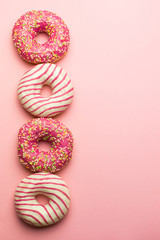 Creative layout made of pink glazed donuts. Flat lay. Food concept. Macro concept. Various decorated doughnuts on soft pink background. Sweet and colourful doughnuts 