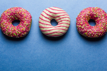Creative layout made of pink glazed donuts. Flat lay. Food concept. Macro concept. Various decorated doughnuts on blue background. Sweet and colourful doughnuts 