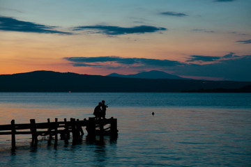 Naklejka na ściany i meble Pesca rilassante su un pontile sul lago calmo al tramonto