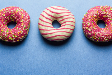 Creative layout made of pink glazed donuts. Flat lay. Food concept. Macro concept. Various decorated doughnuts on blue background. Sweet and colourful doughnuts 