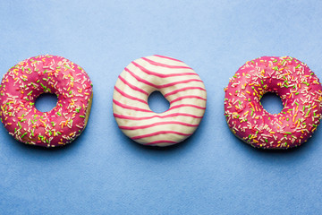 Creative layout made of pink glazed donuts. Flat lay. Food concept. Macro concept. Various decorated doughnuts on blue background. Sweet and colourful doughnuts 