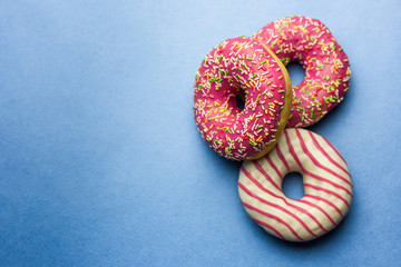 Creative layout made of pink glazed donuts. Flat lay. Food concept. Macro concept. Various decorated doughnuts on blue background. Sweet and colourful doughnuts 