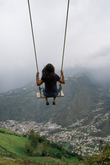 Beautiful young woman on the swing. Swinging over beautiful mountain. Banos, Ecuador.