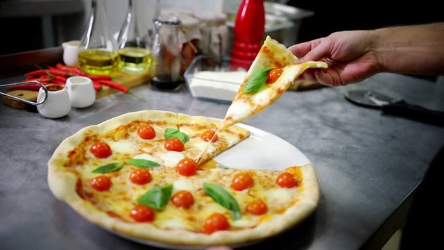 Restaurant kitchen. A chef takes a piece of Caesar pizza