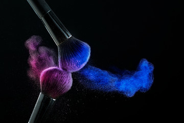 Cosmetic shades of different colors, red and blue, fly away from two make-up brushes creating a...