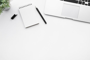 White office desk table with blank notebook page with pen and laptop computer. Top view with copy space, flat lay.