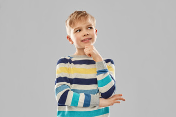childhood, expressions and people concept - portrait of smiling little boy in striped pullover thinking over grey background